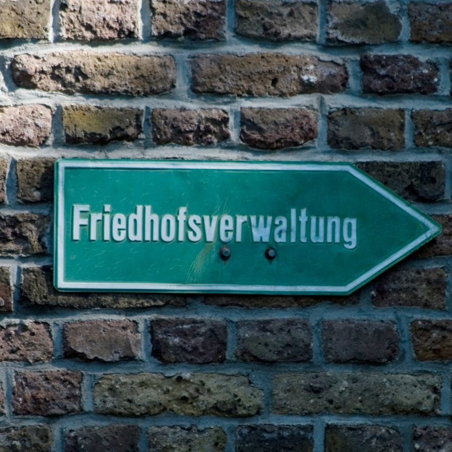 Grünes Schild an einer Mauer mit der Aufschrift Friedhofsverwaltung