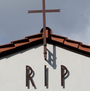 Friedhofskapelle mit Kreuz am Dach und der Aufschrift RIP