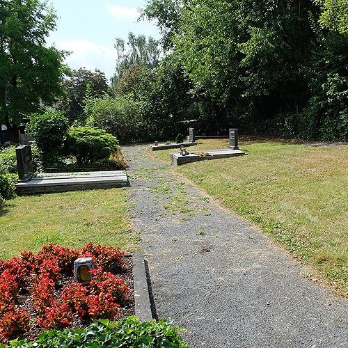 Einzelne Gräber auf fast leerer Fläche an einem Weg auf einem Friedhof