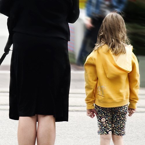 Kind mit gelber Jacke neben erwachsener Frau mit schwarzer Kleidung