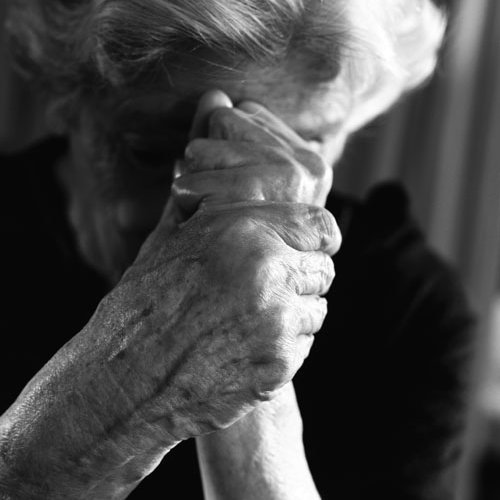 Ältere Frau senkt den Kopf und faltet die Hände vor ihrem Gesicht