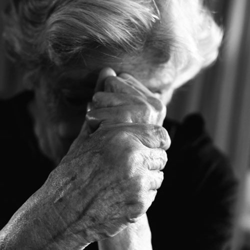 Ältere Frau senkt den Kopf und faltet die Hände vor ihrem Gesicht