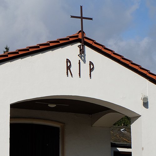 Trauerhalle mit Kreuz auf dem Dach und Schrift RIP auf dem Giebel